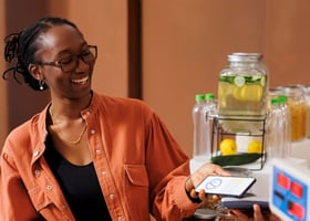 Middle-aged African American woman in orange jacket using her cellphone's mobile wallet to pay at a coffee shop.