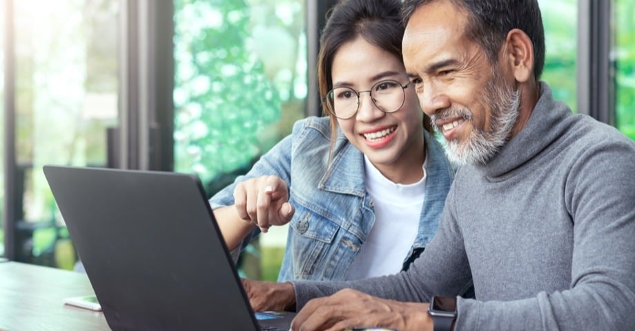 Young woman helping older man navigate laptop