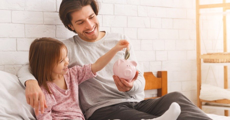 Father and daughter putting money into a pink piggy bank