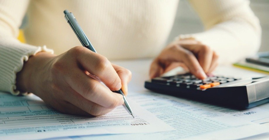 Person writing on paper and using a calculator, just hands shown