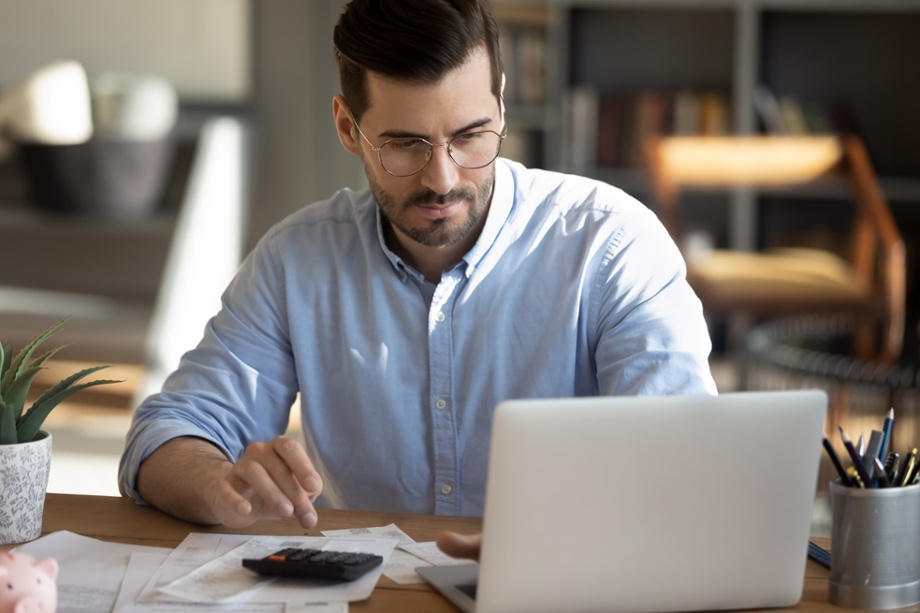 Man looking at a laptop and using a calculator 