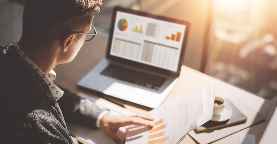 Man working at a laptop with charts and data on the screen