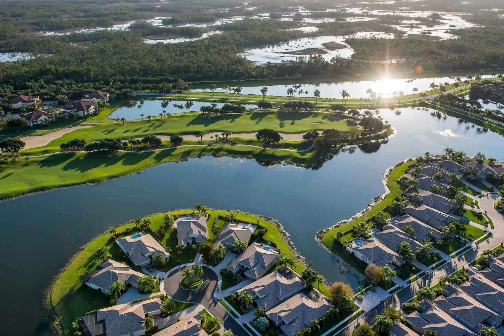 Modern housing development surrounded by water with a sun flare in the top right corner