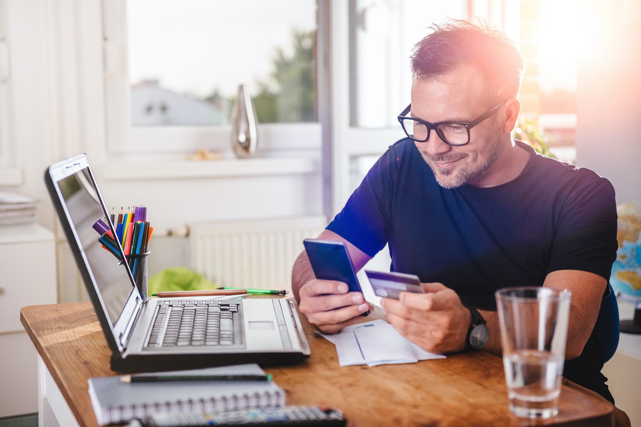 Man in glasses smiling while entering card information into his phone