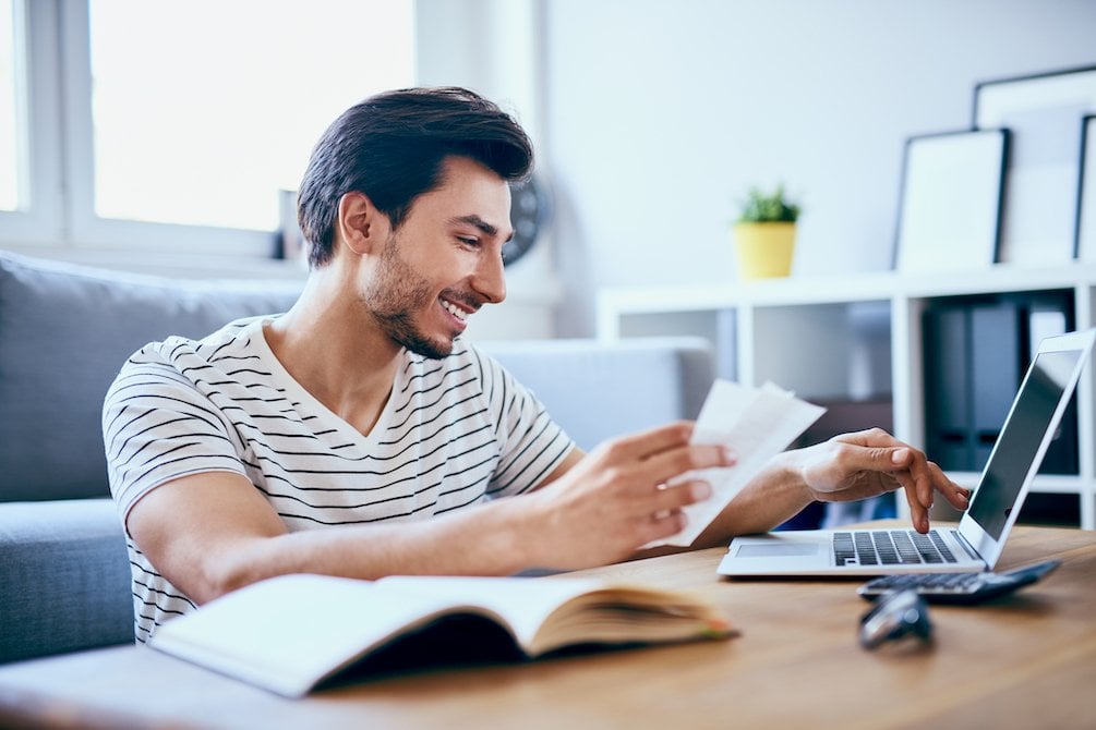 Young man smiling looking at receipts and his laptop