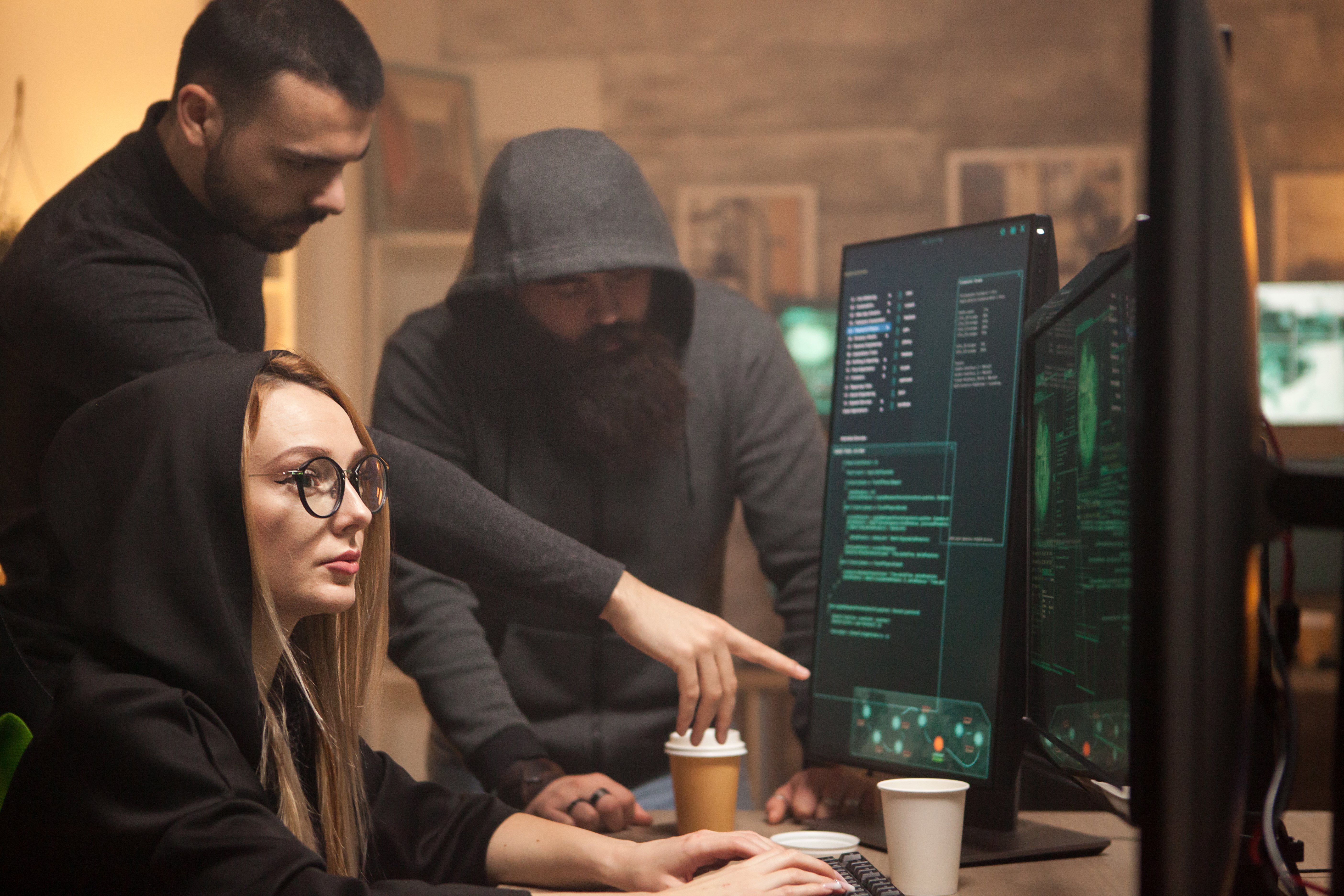 People in dark clothes looking at a screen representing hackers