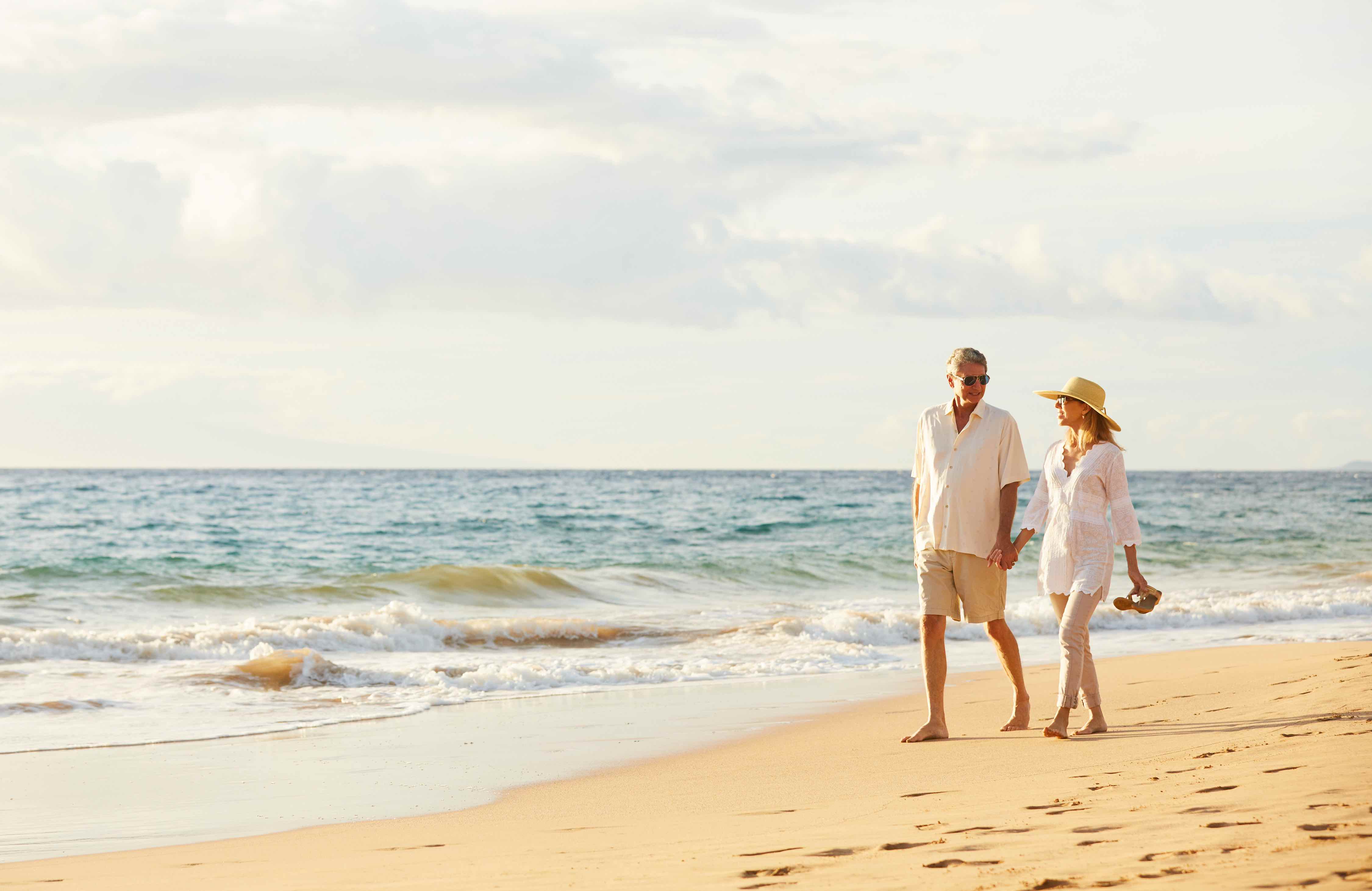 Older couple holding hands and walking along the beach