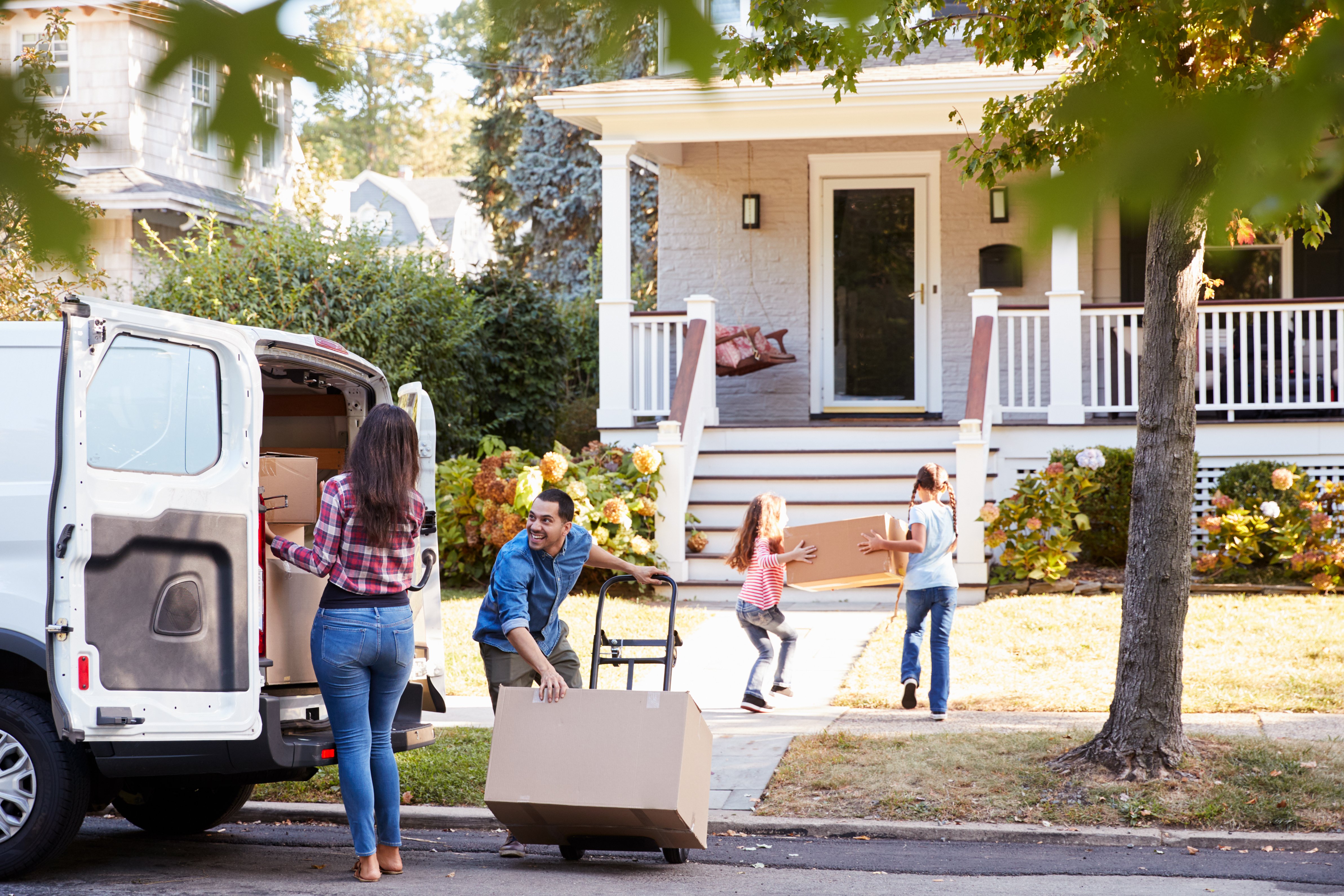 A family of four unpacks a moving truck and carries boxes into their new home.